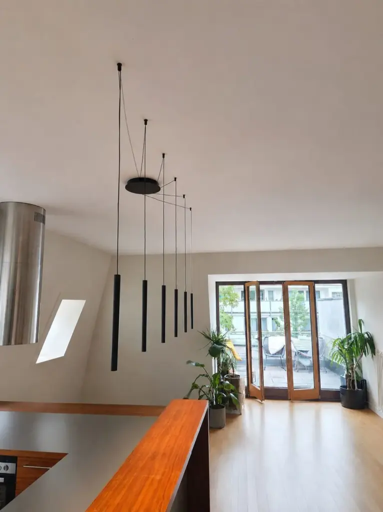 Mehrere schlanke schwarze Pendelleuchten an einem gemeinsamen Deckenbaldachin in einer hellen Dachgeschosswohnung