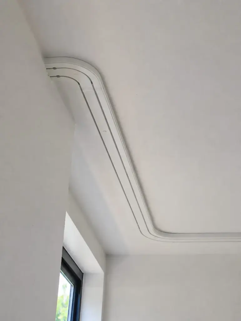 Weiße zweiläufige Vorhangschiene, entlang einer Deckenkante um die Ecke montiert